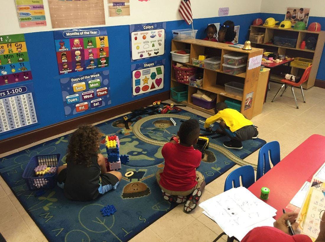 Three children playing on a rug in a classroom