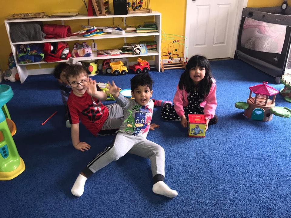 Three children playing on a blue carpeted floor in a room with toys