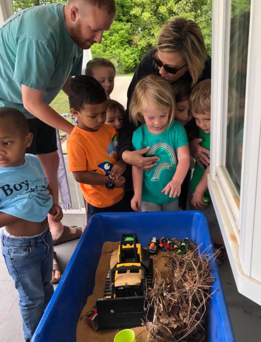 Adults and children looking at toy construction vehicles in a blue bin