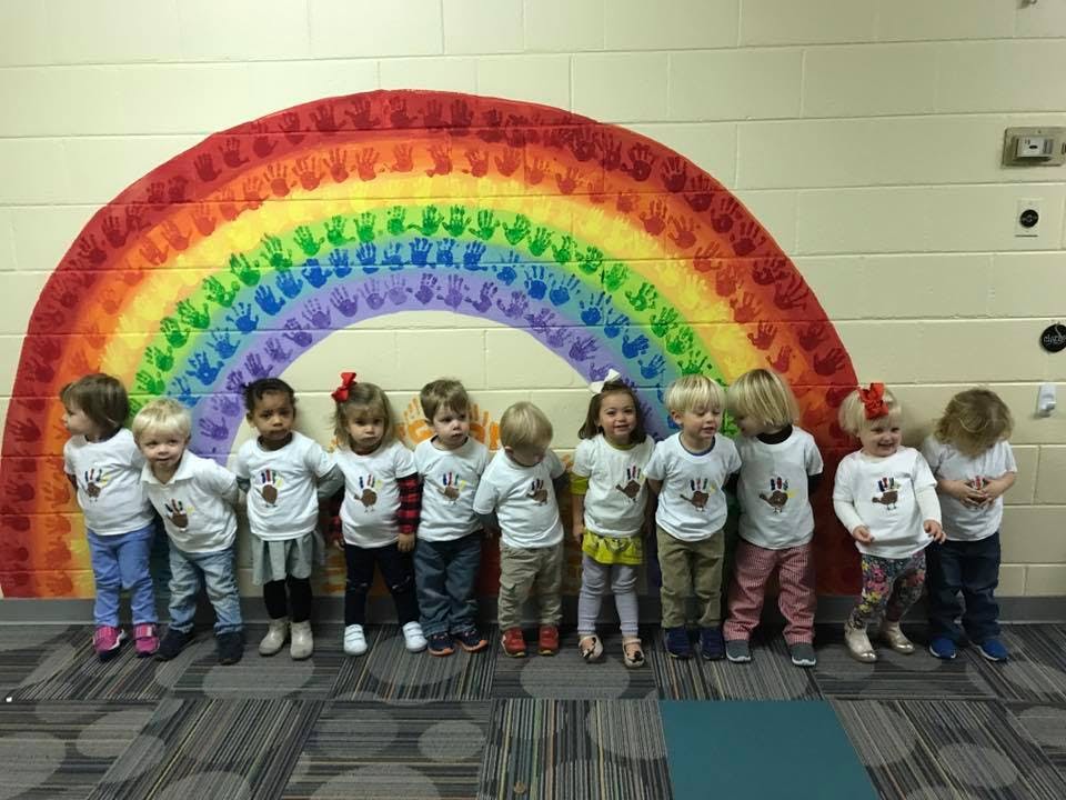 Group of children standing in front of a rainbow mural