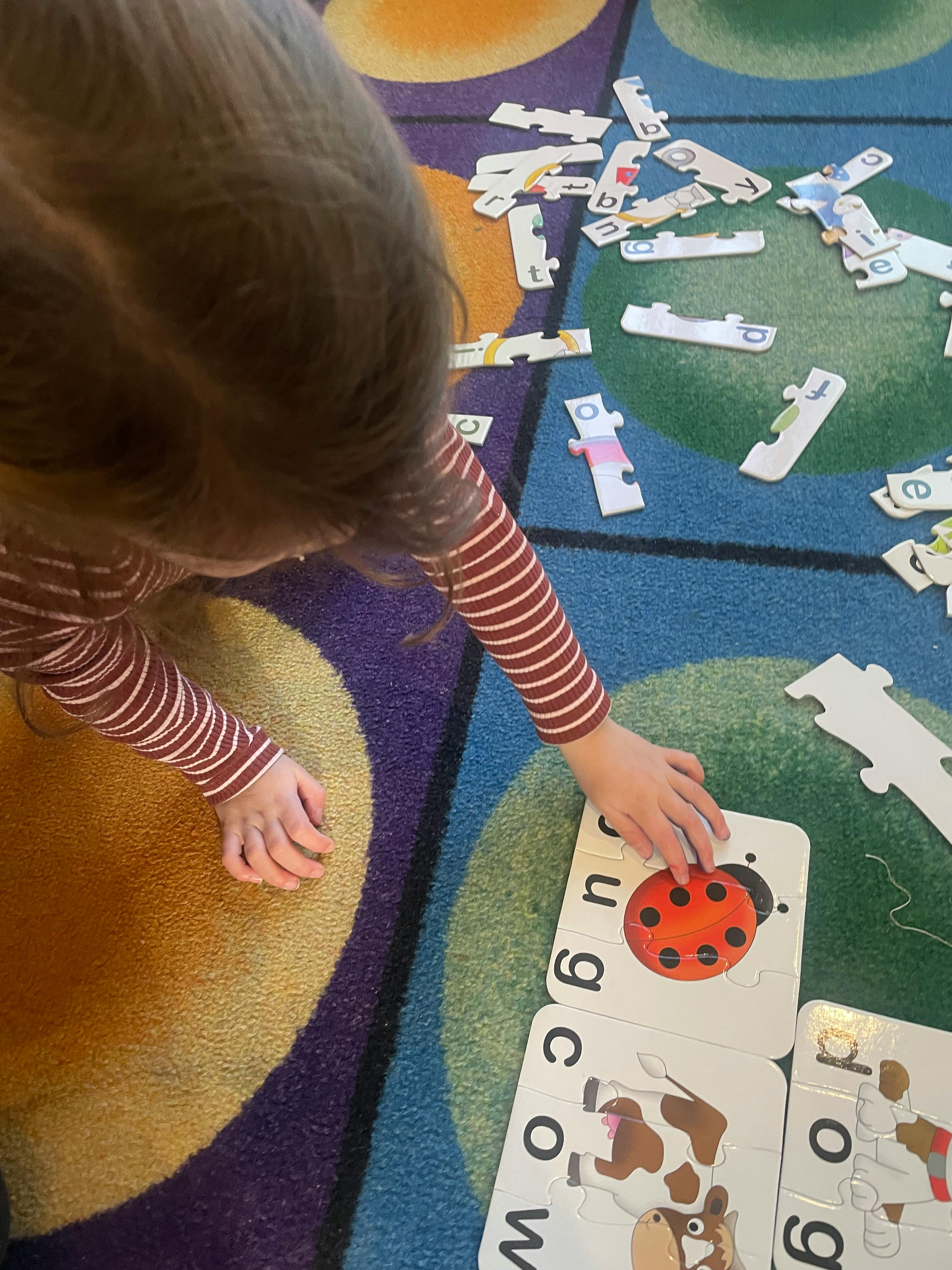 Child playing with alphabet puzzle pieces on a colorful rug
