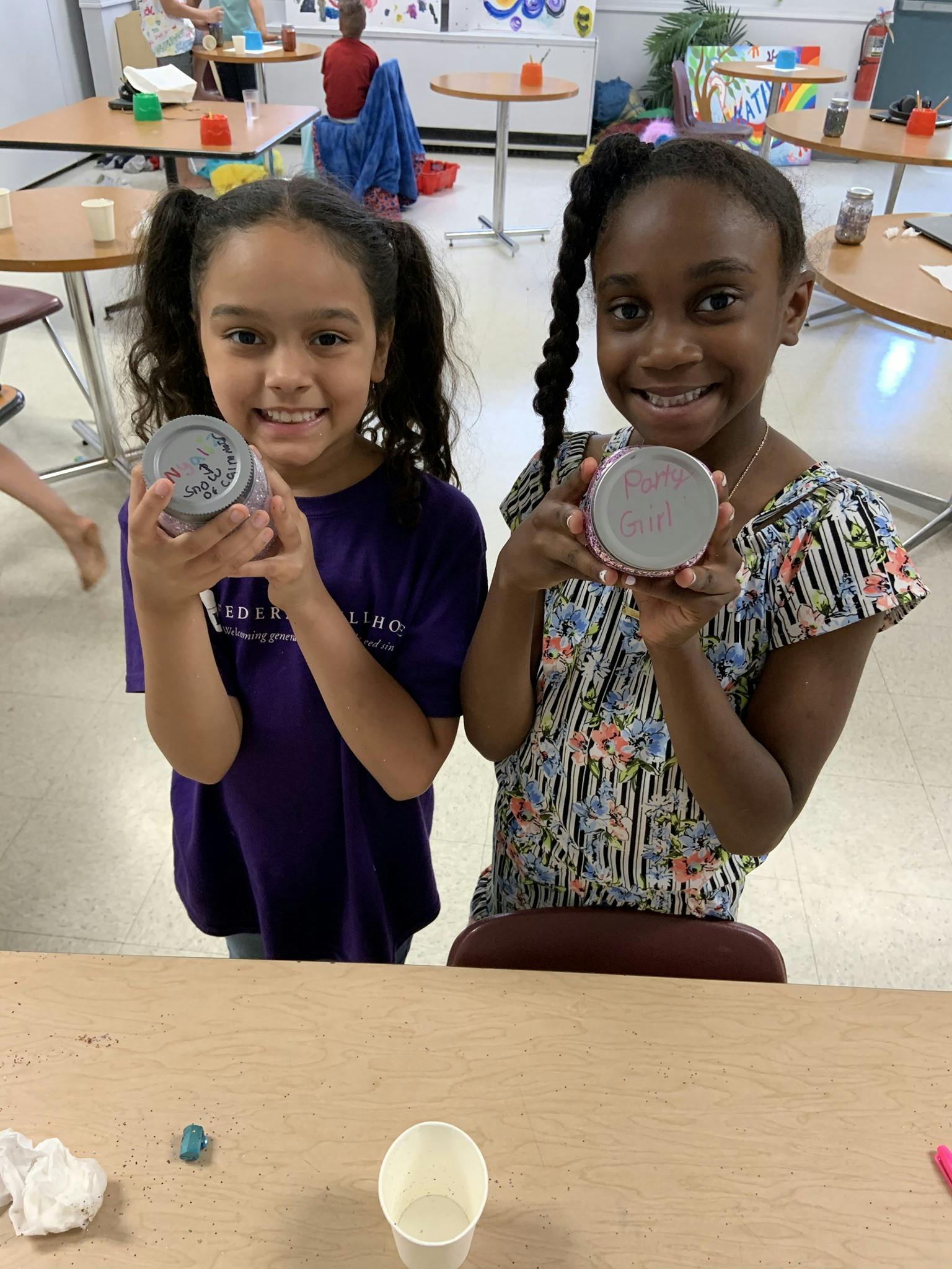 Two children holding up small round containers
