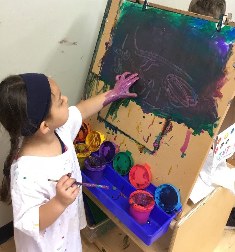 Child painting on an easel with their hand and a paintbrush