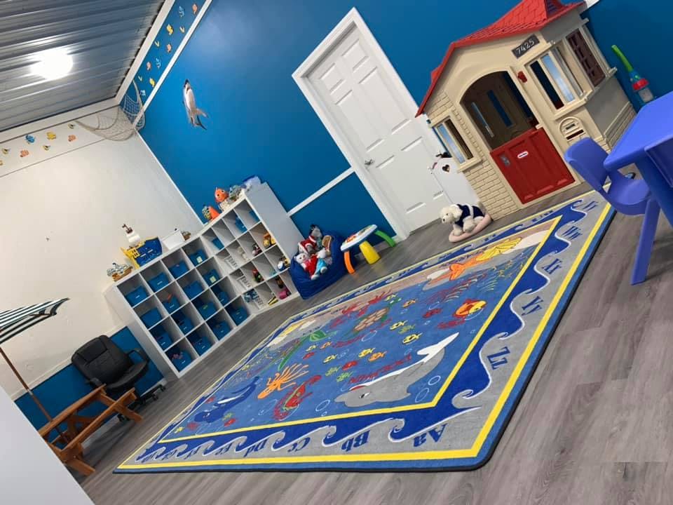 Playroom with a blue rug, toy house, and storage shelves