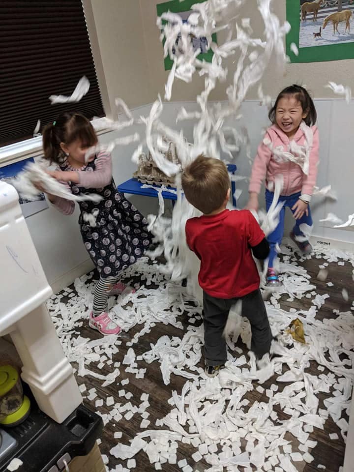 Three children playing in a room filled with shredded paper