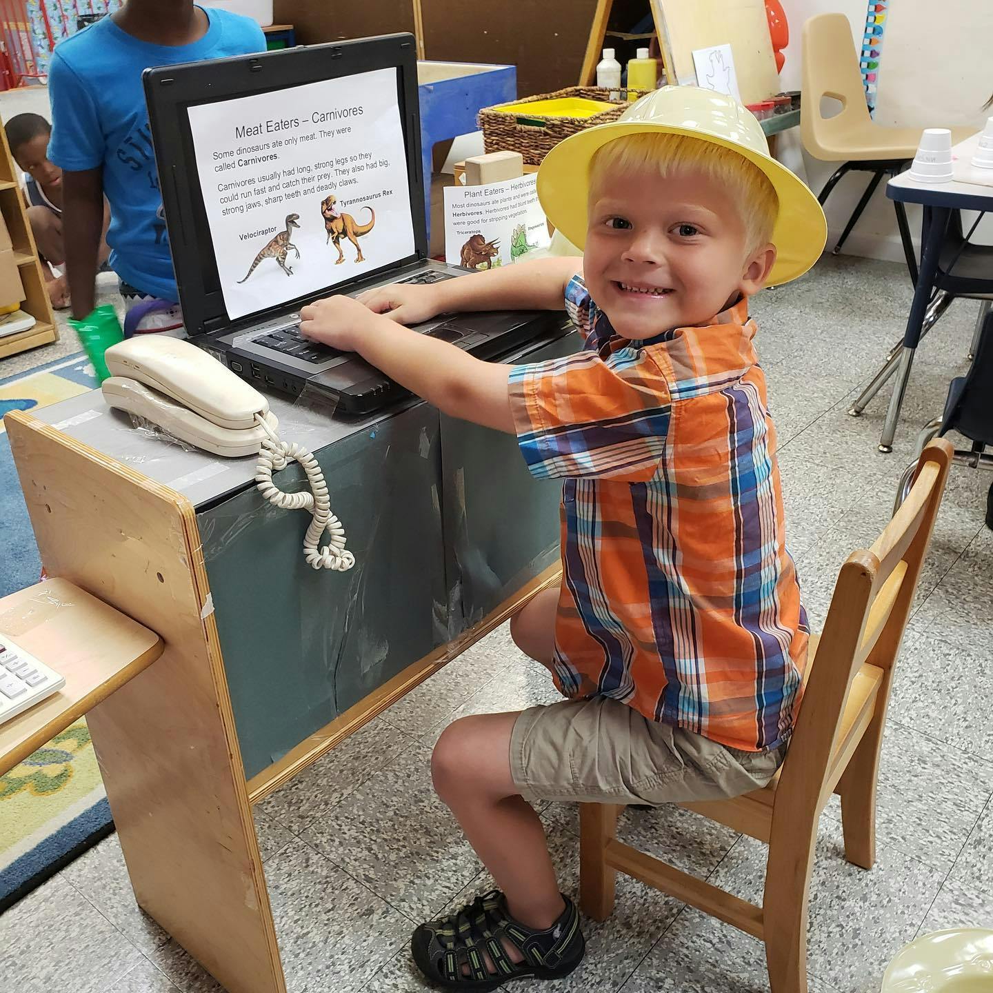 Child in a hat using a laptop in a classroom