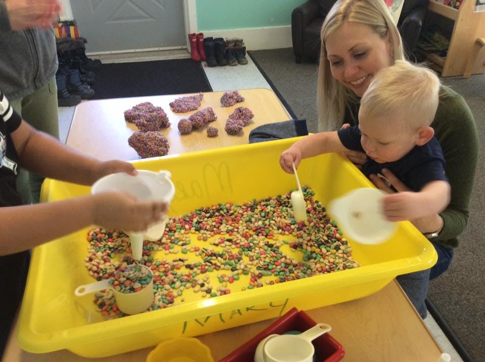 Adult and two children playing with sensory bin in a classroom