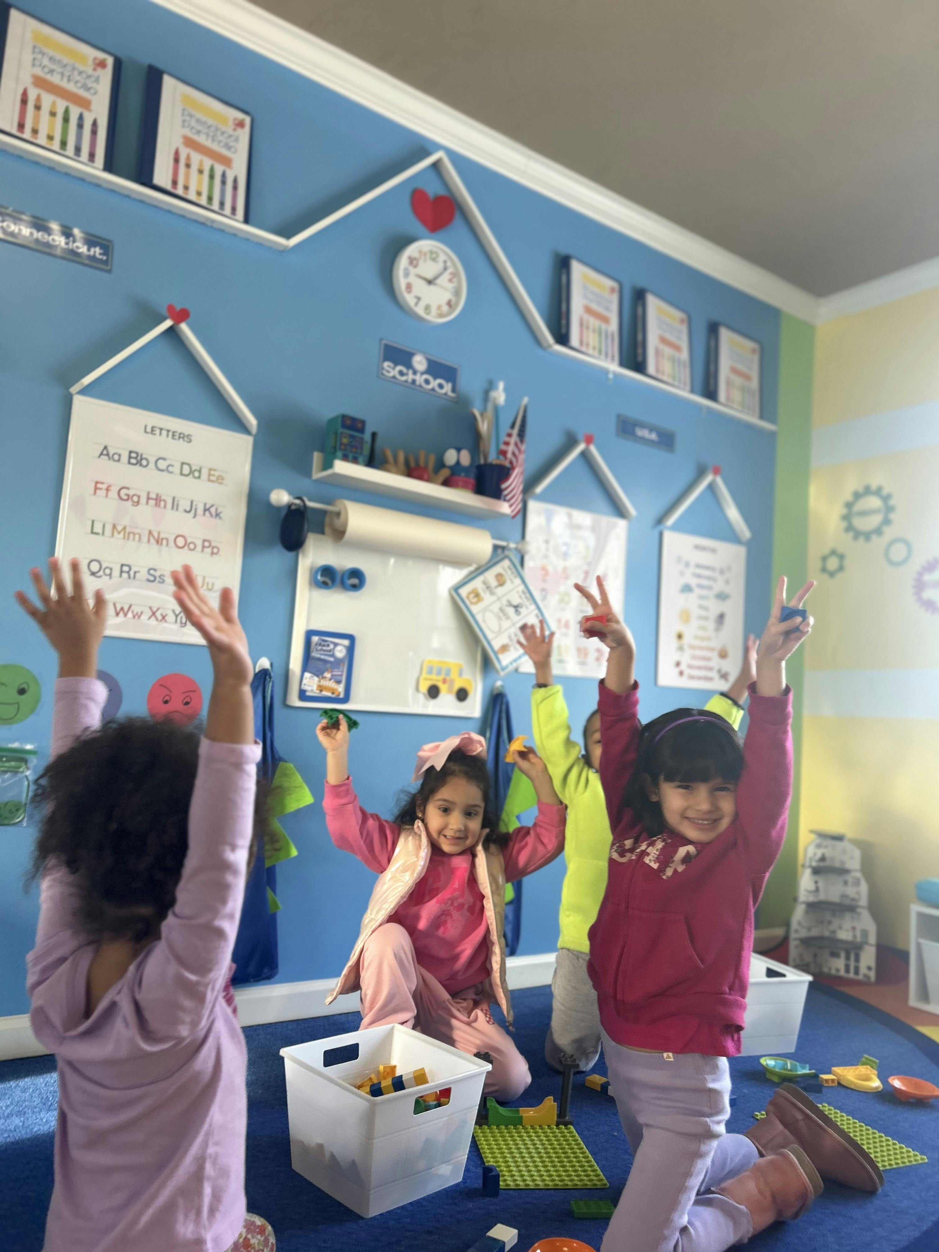 Children playing with toys in a classroom with their arms raised