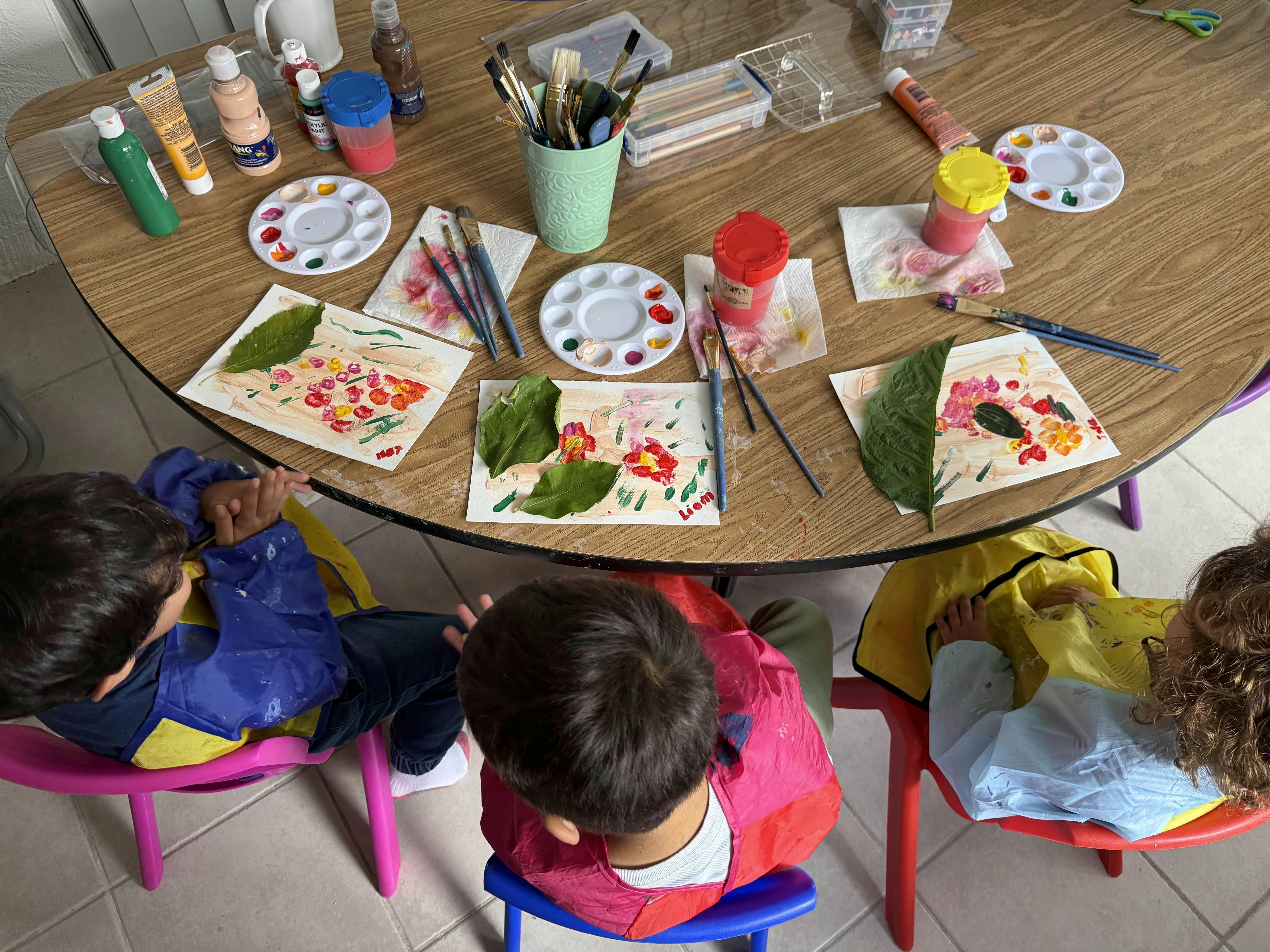 Three children in smocks painting with leaves on a table