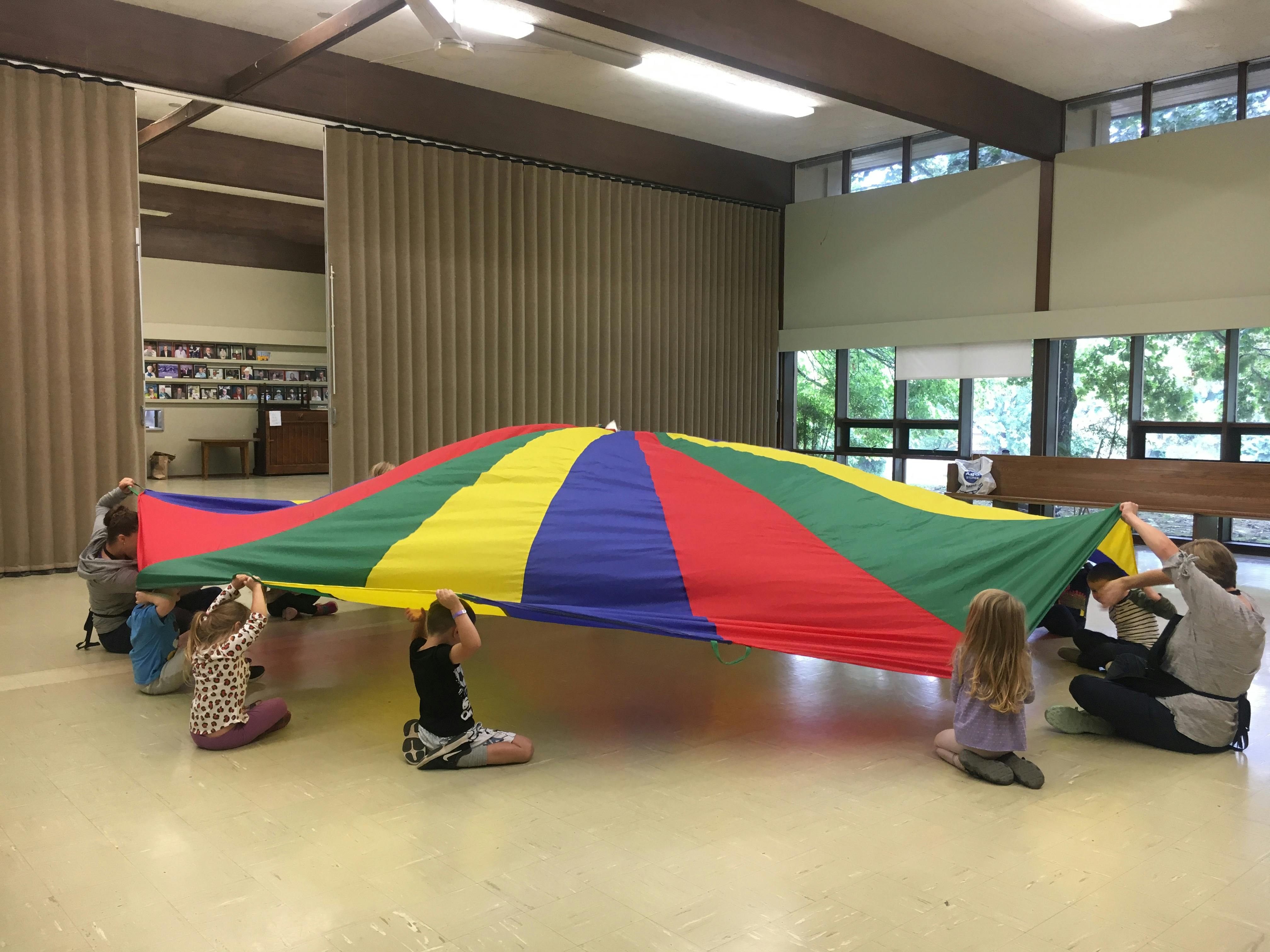People and children playing with a large colorful parachute