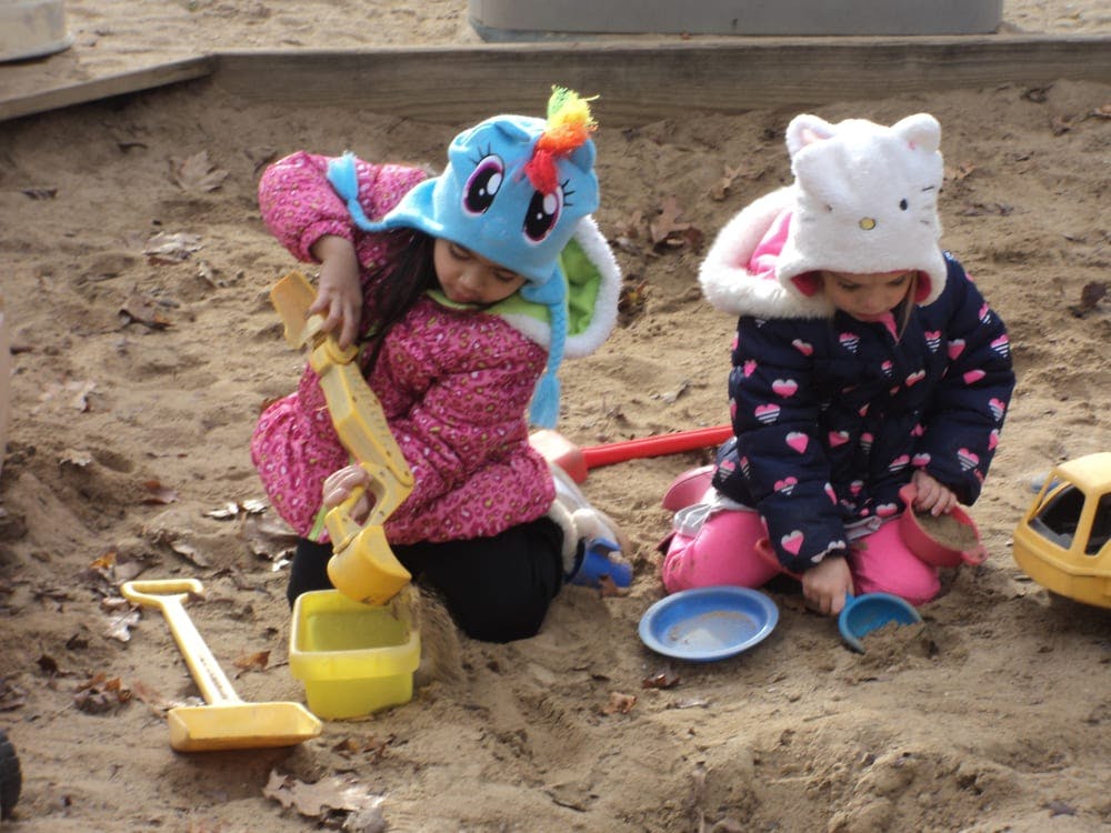 Two children playing in a sandbox with toys