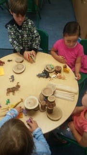 Children playing with animal figurines and wooden blocks at a round table