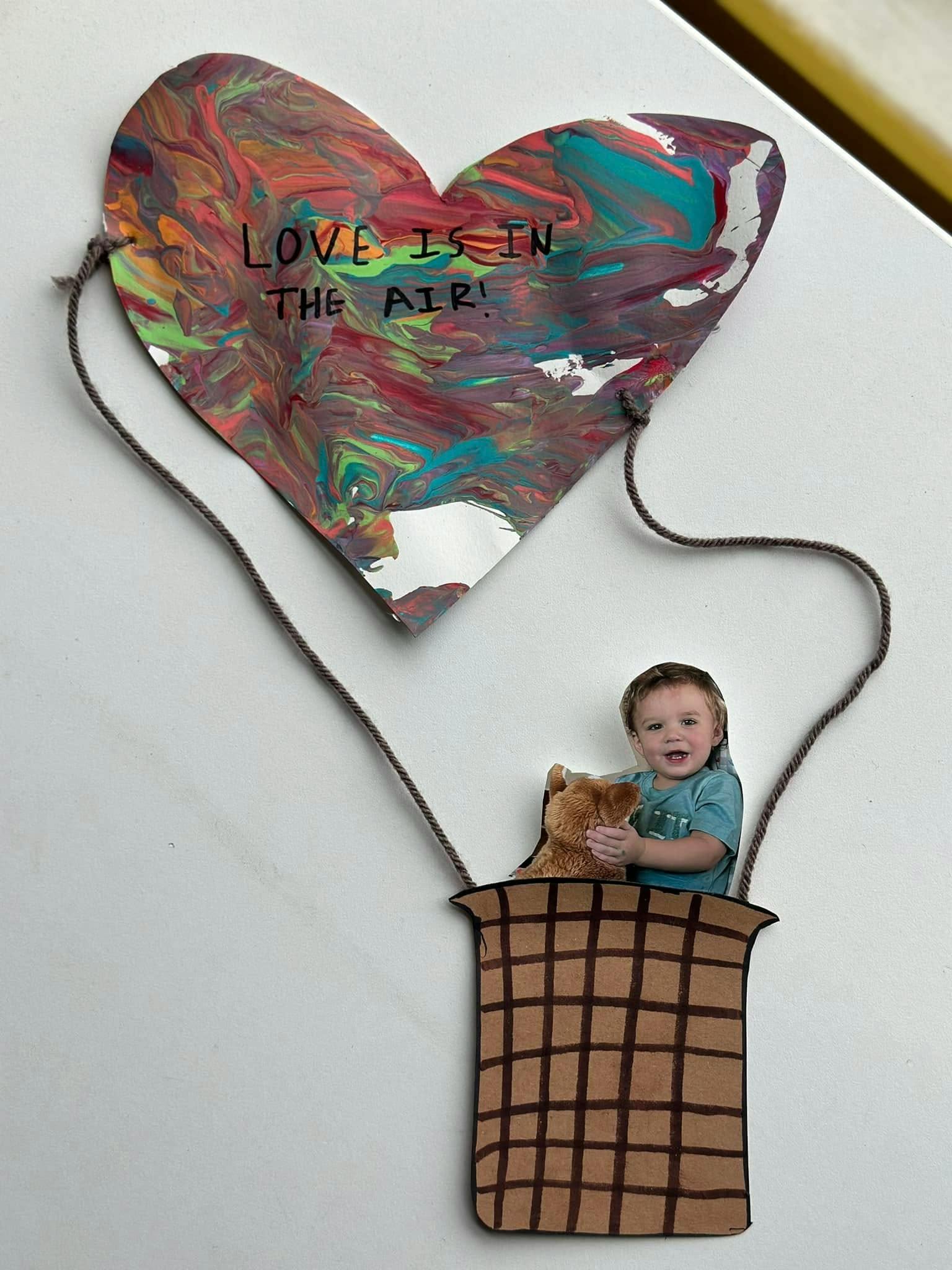 Child in a hot air balloon craft with "LOVE IS IN THE AIR!" on the balloon