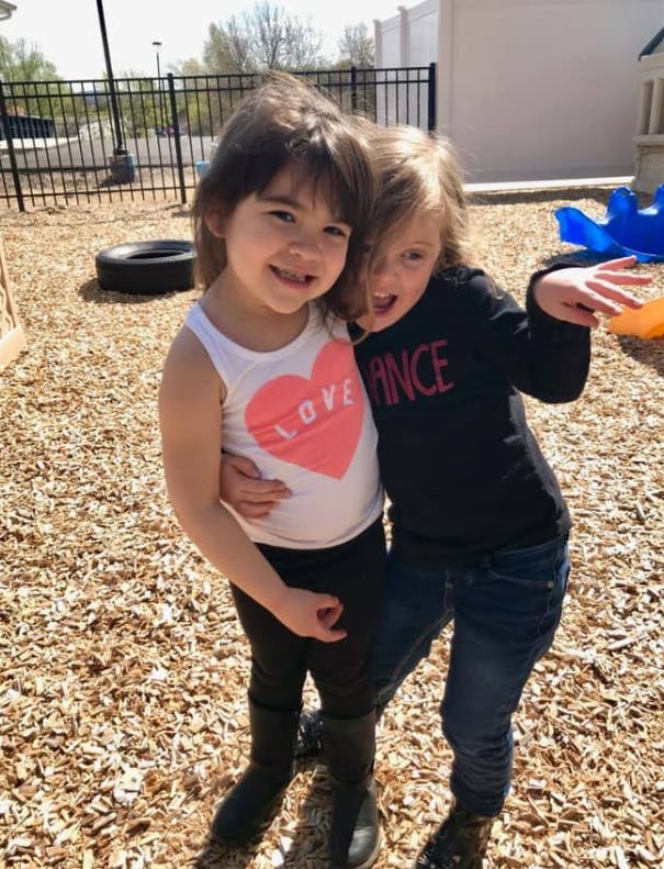 Two children standing close together on wood chips