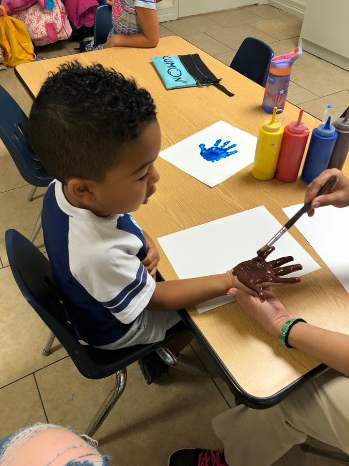 Child having their hand painted brown at a table