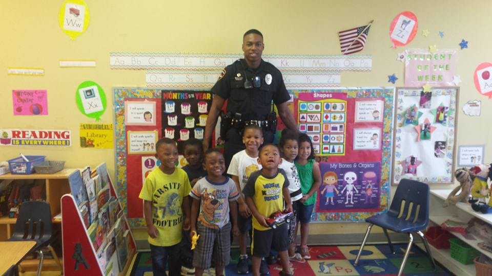 Person in uniform standing with several children in a classroom