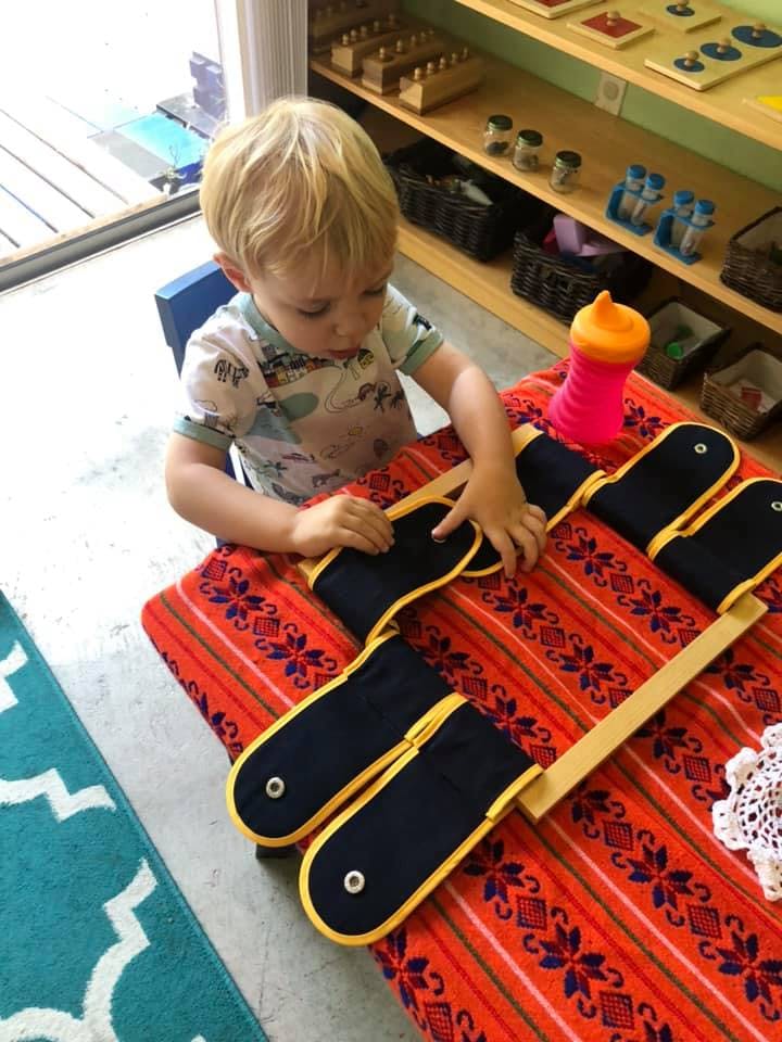 Child playing with a dressing frame on a table