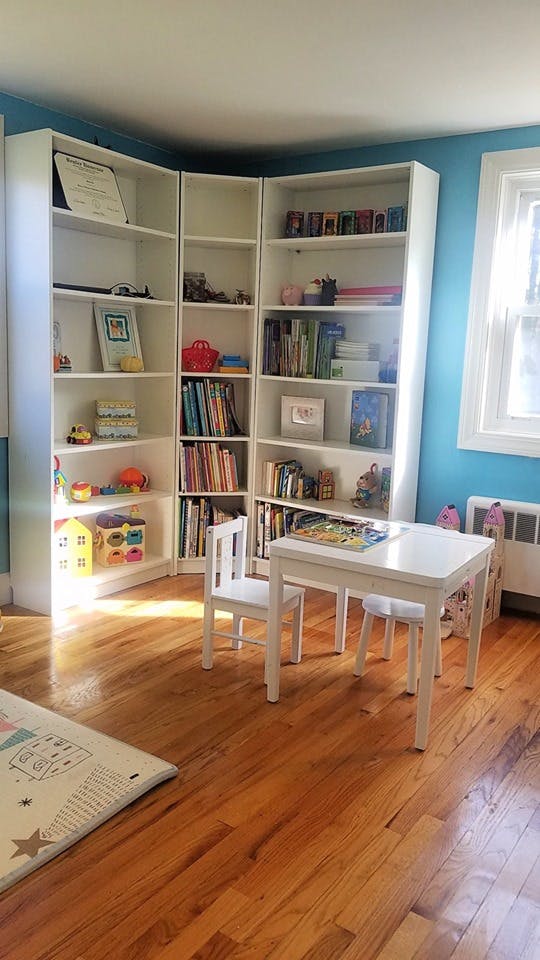Corner bookshelves with books and toys next to a child's table and chairs