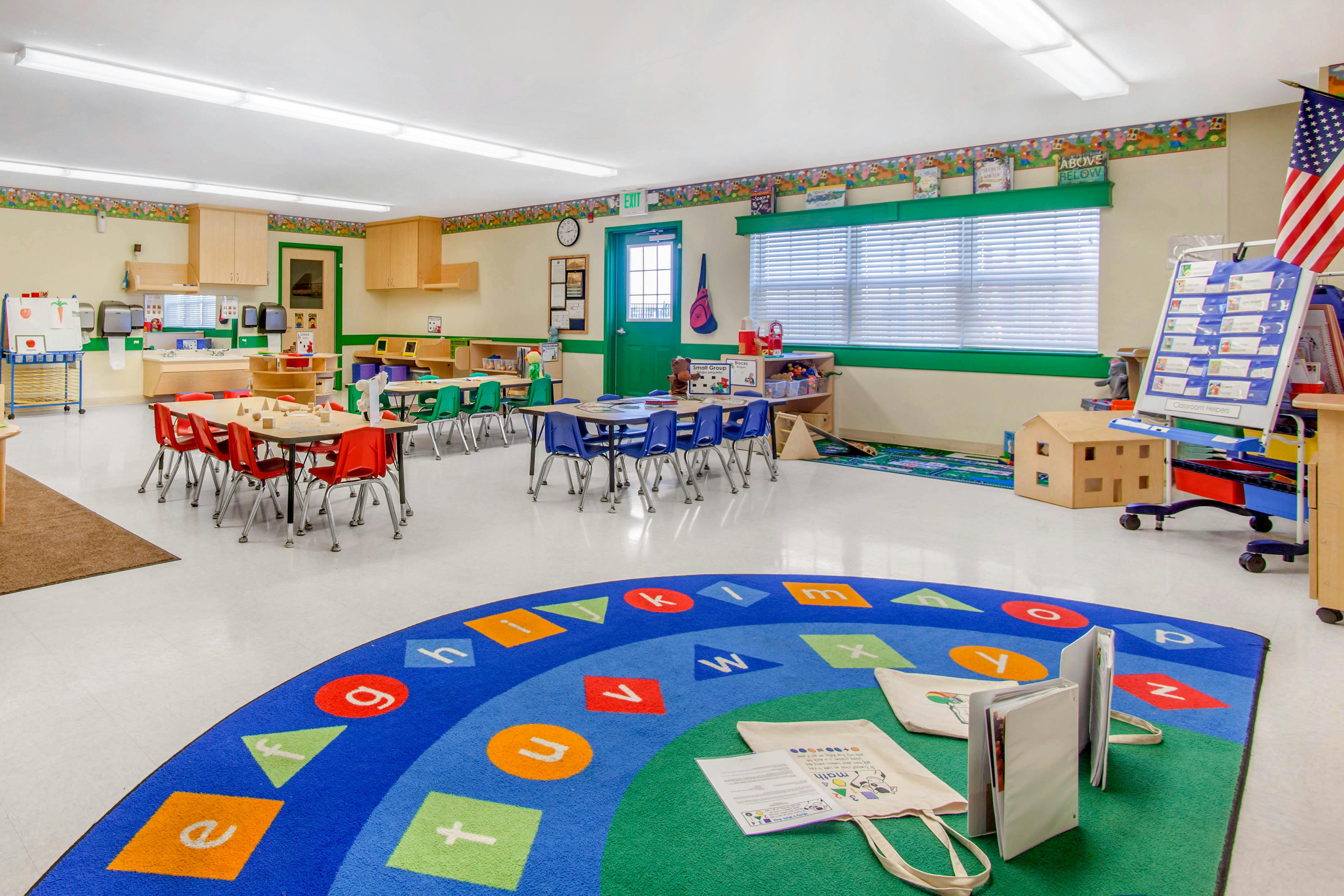 Classroom with small tables and chairs, a large alphabet rug, and teaching aids