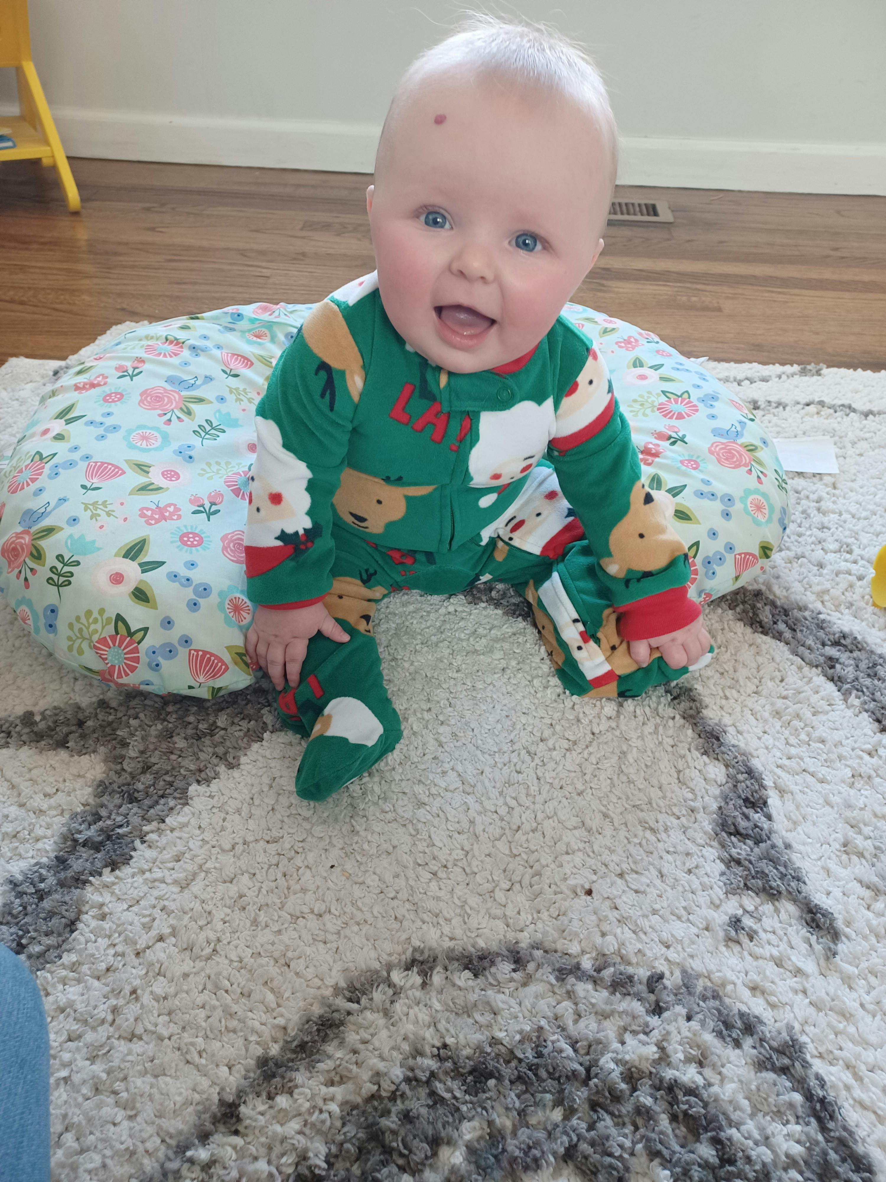 Child in green pajamas sitting on a patterned pillow