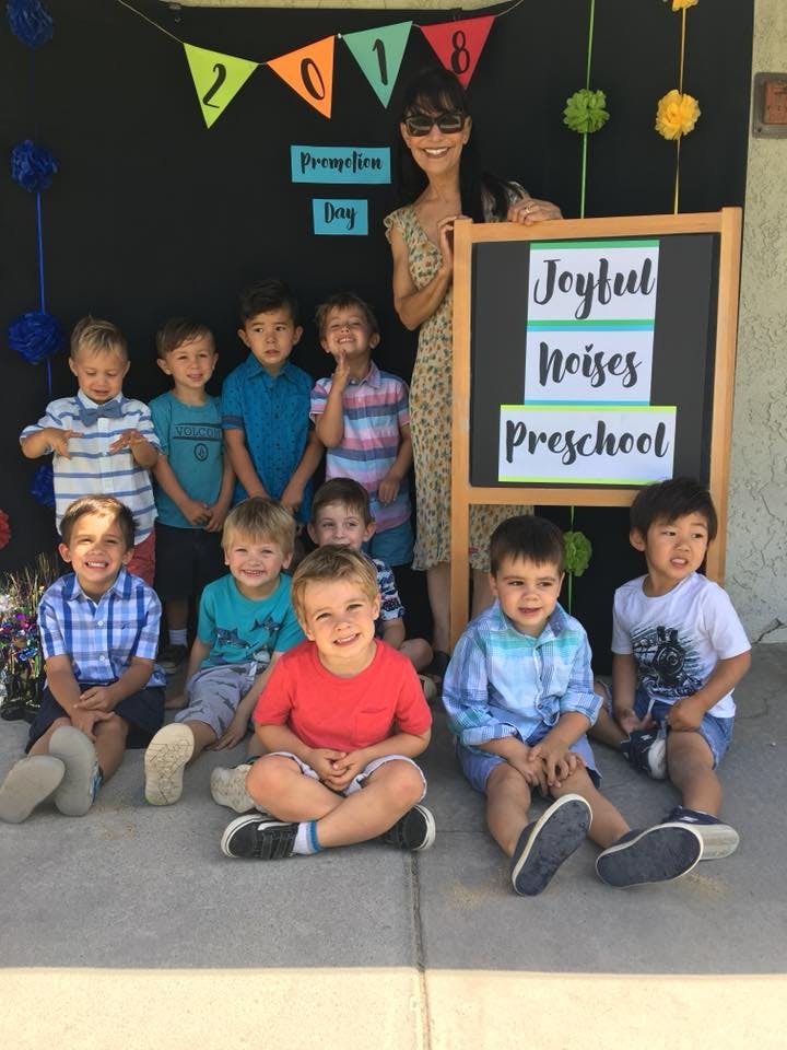Adult and children posing in front of a sign that reads "Joyful Noises Preschool"