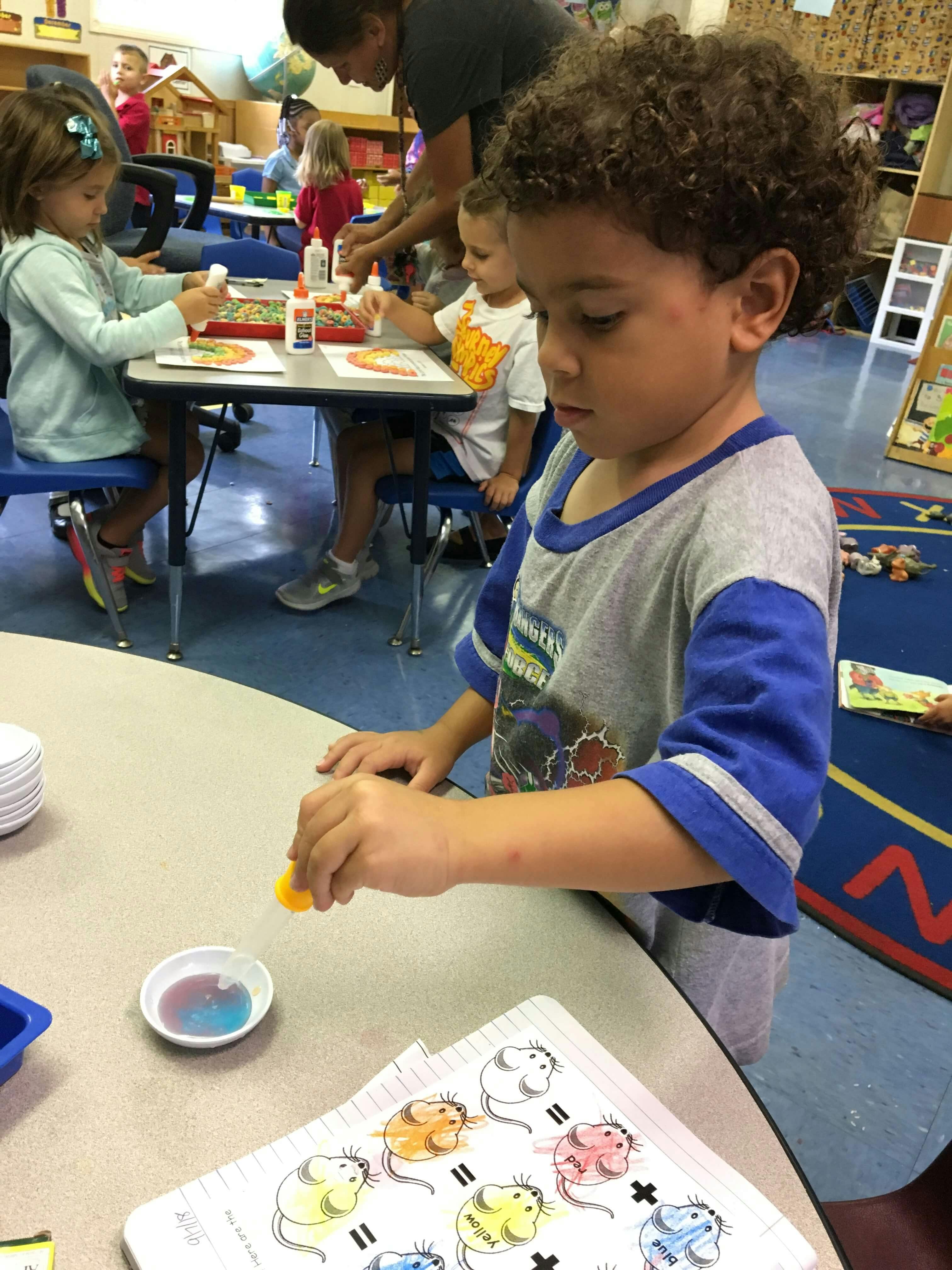 Child using a dropper with liquid at a table in a classroom
