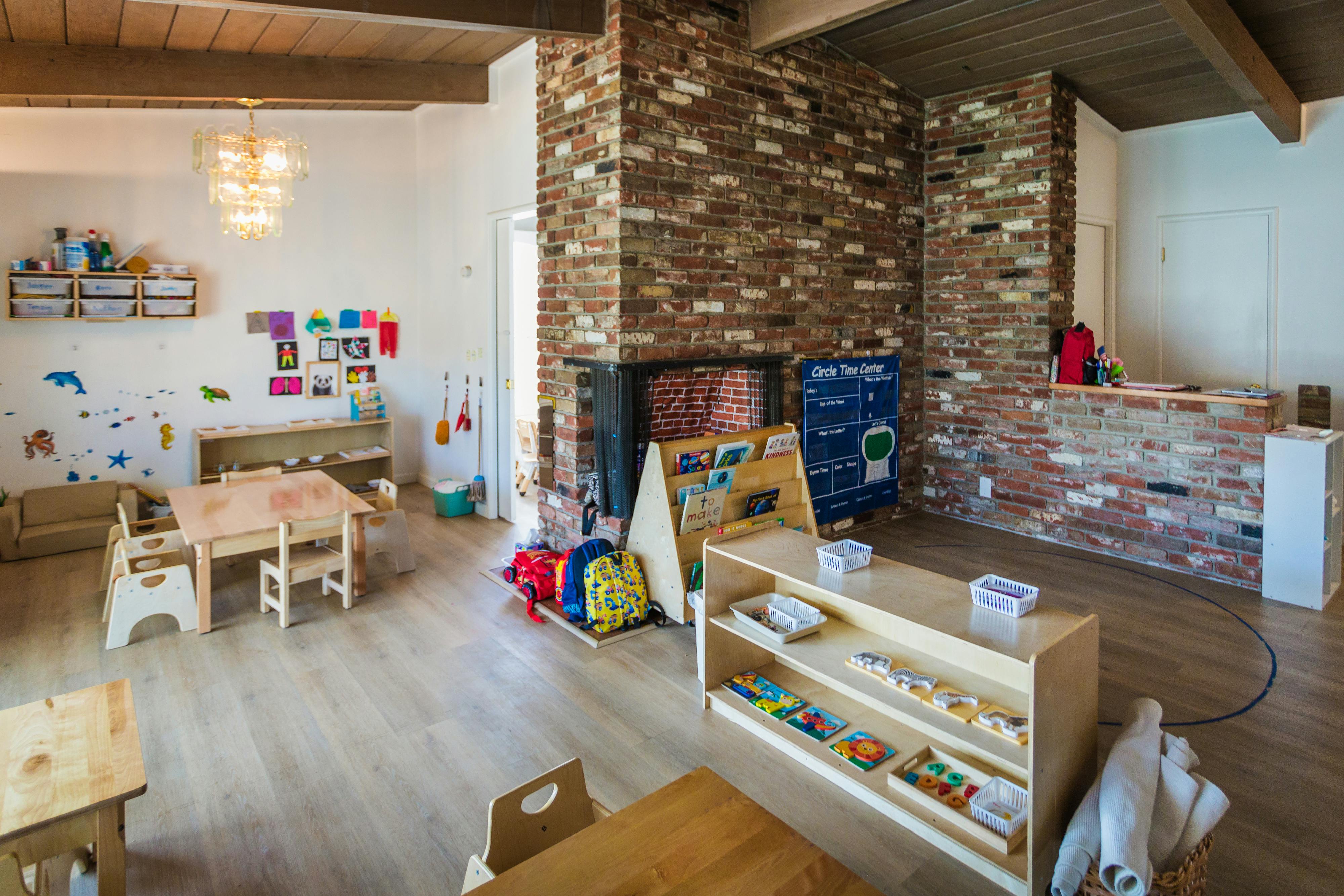 Classroom with small wooden tables and chairs, shelves with learning materials