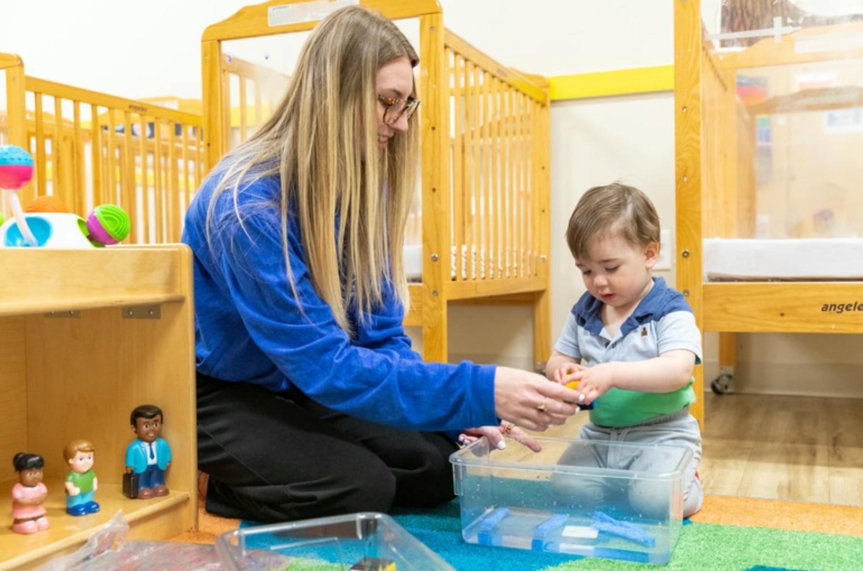 Adult and child playing with water in a clear container on the floor