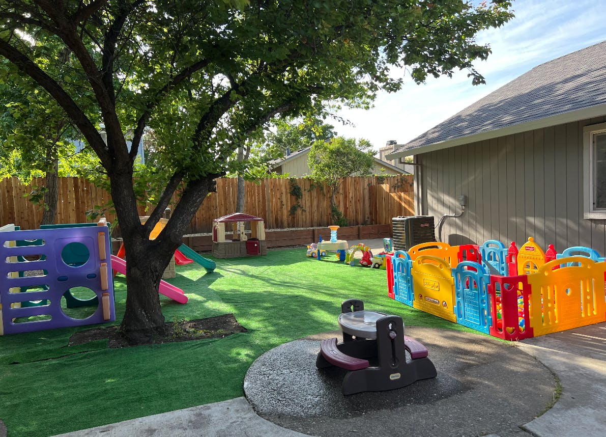 Outdoor play area with artificial grass, tree, and colorful play structures
