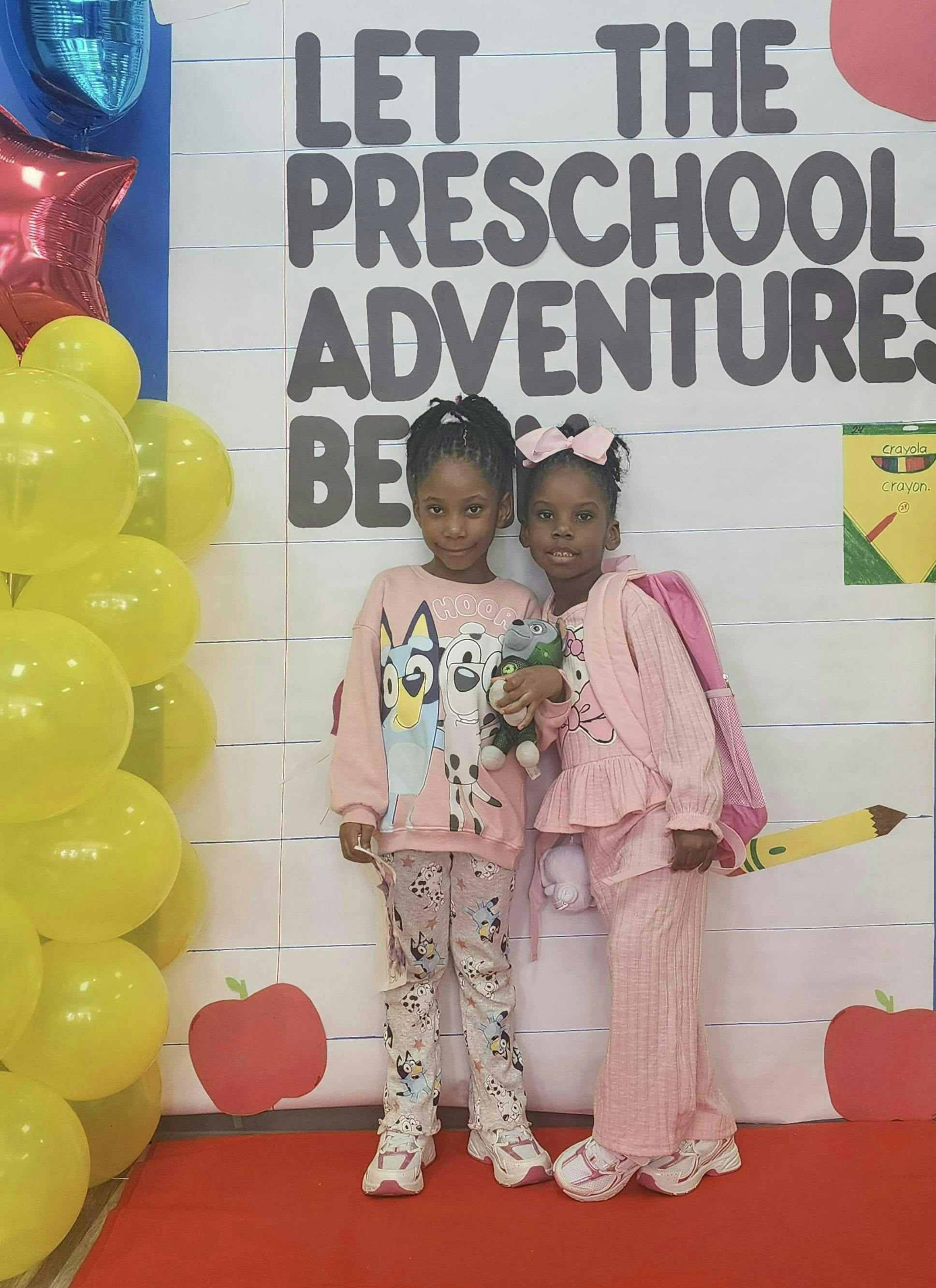 Two children standing in front of a sign that says "Let the Preschool Adventures Begin"
