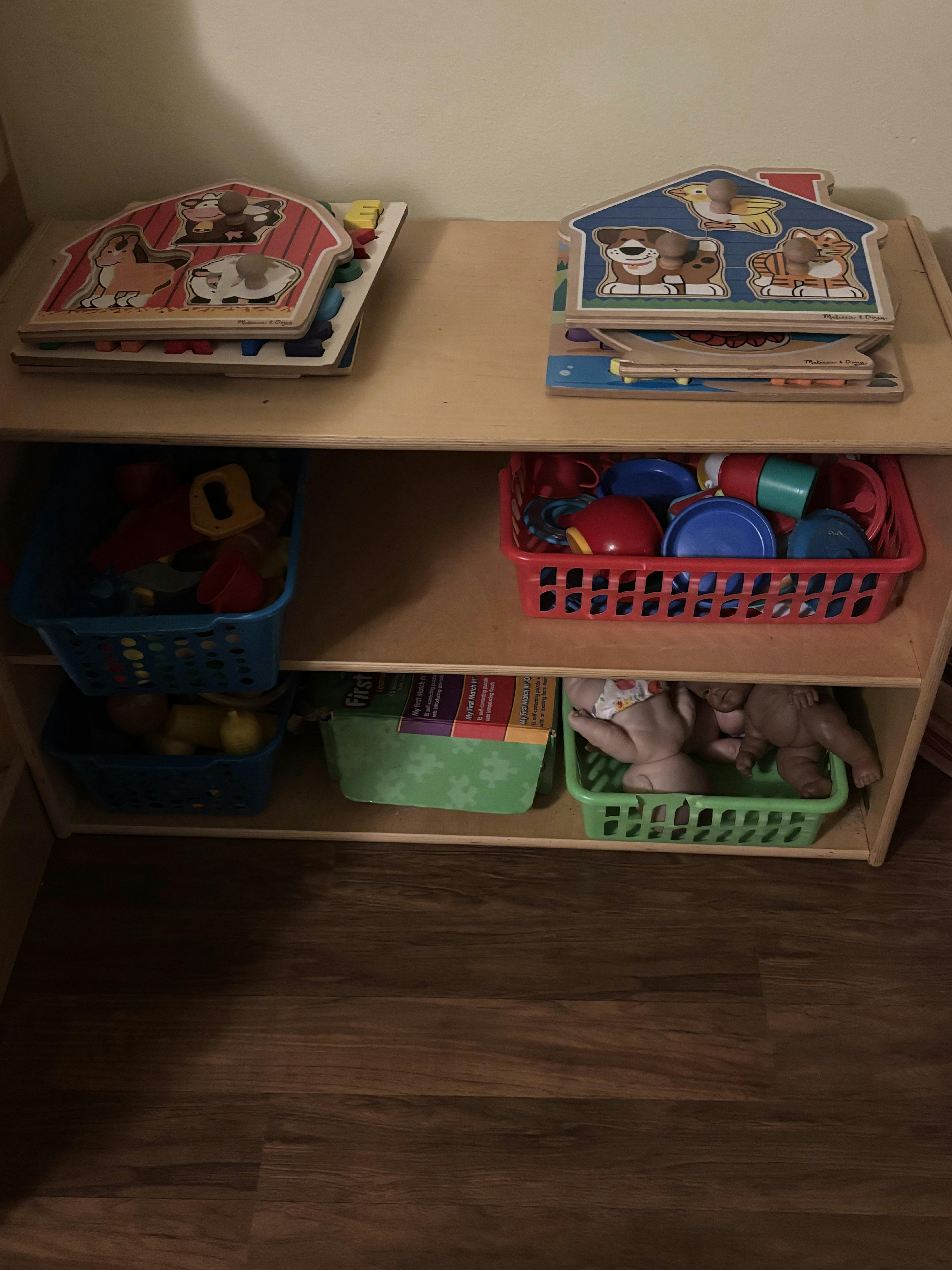 wooden shelves with puzzles, toy dishes, boxes of games, and baby dolls