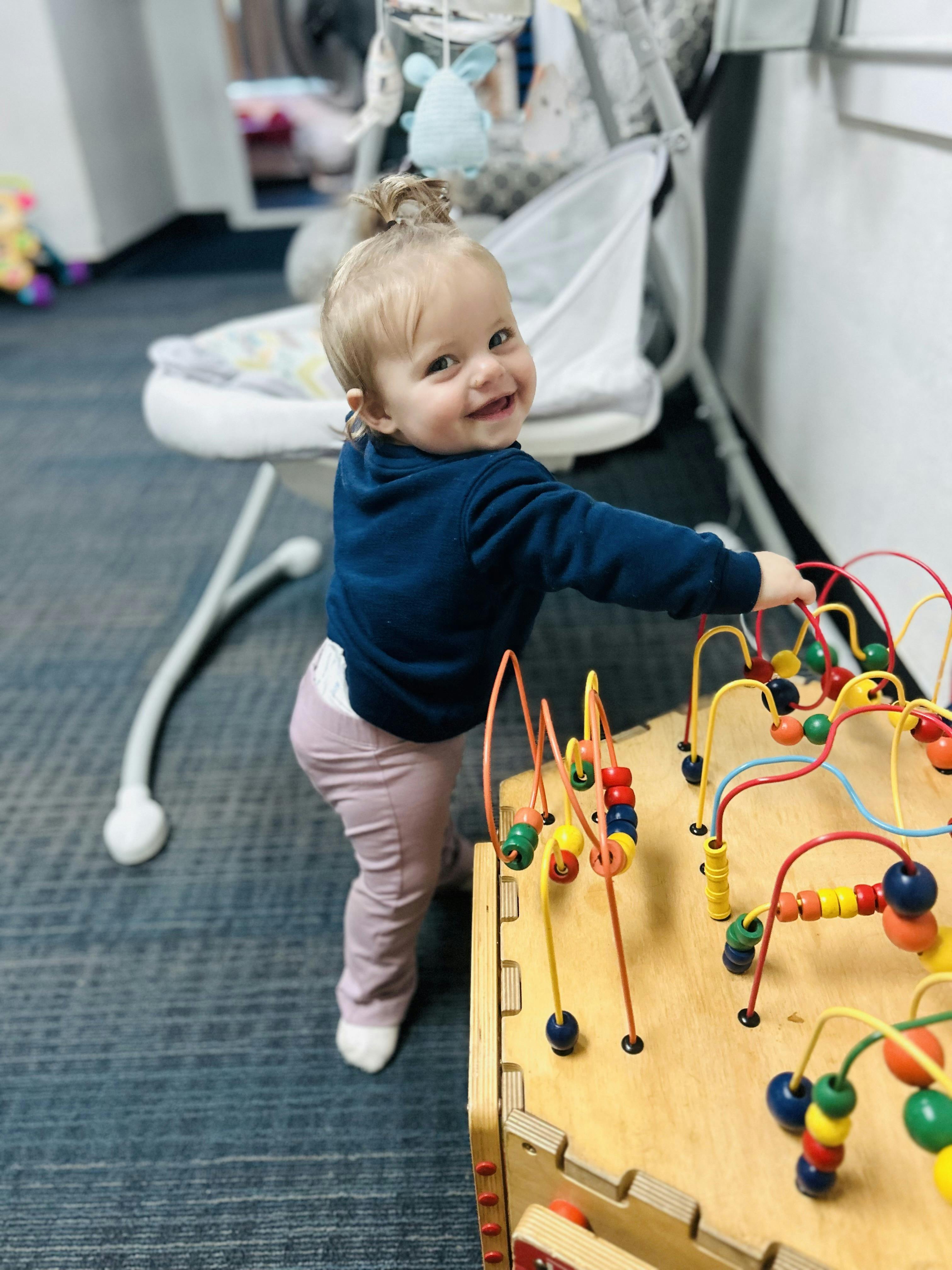 Child playing with a bead maze toy, looking over their shoulder at the camera