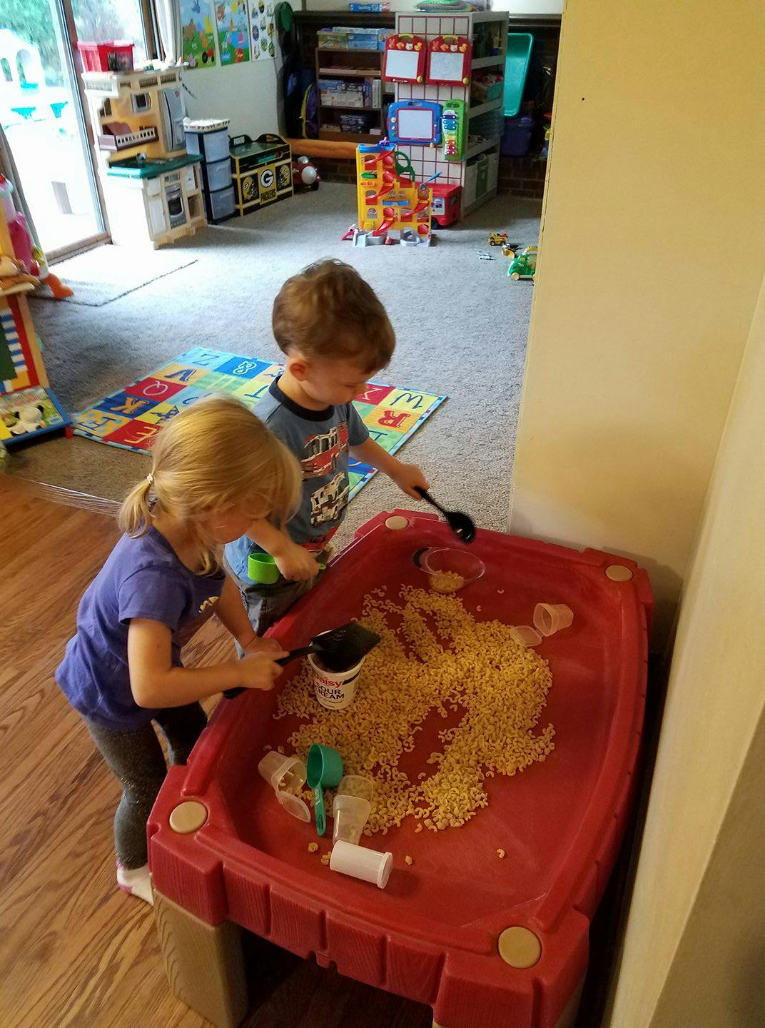 Two children playing with a sensory table filled with pasta