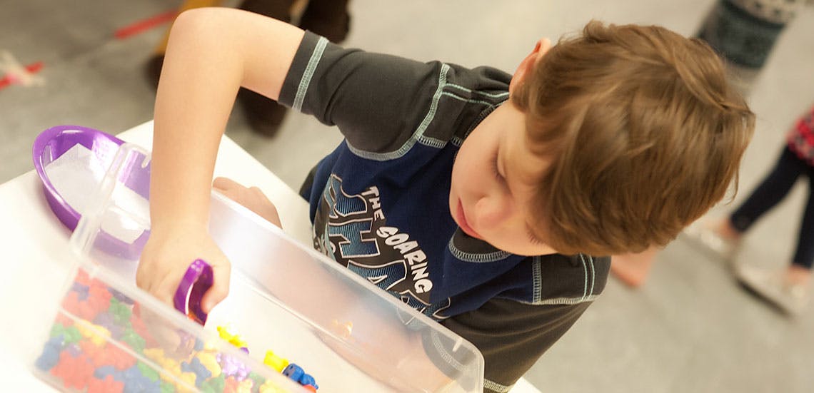 Child playing with colorful beads in a clear container