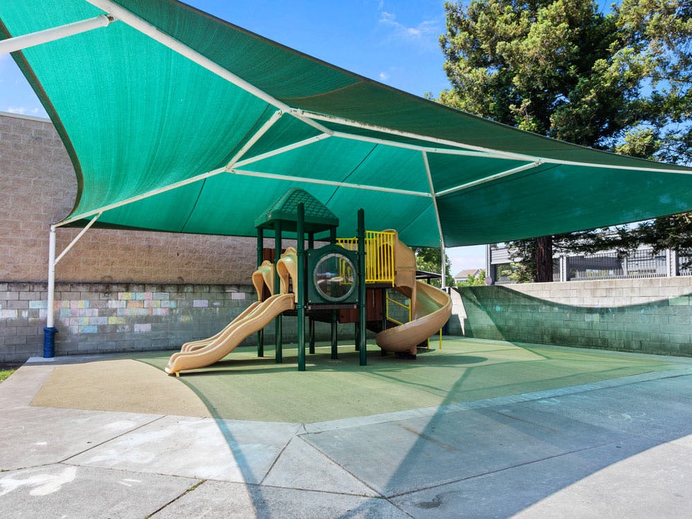 Playground with slides and climbing structures under a green shade canopy