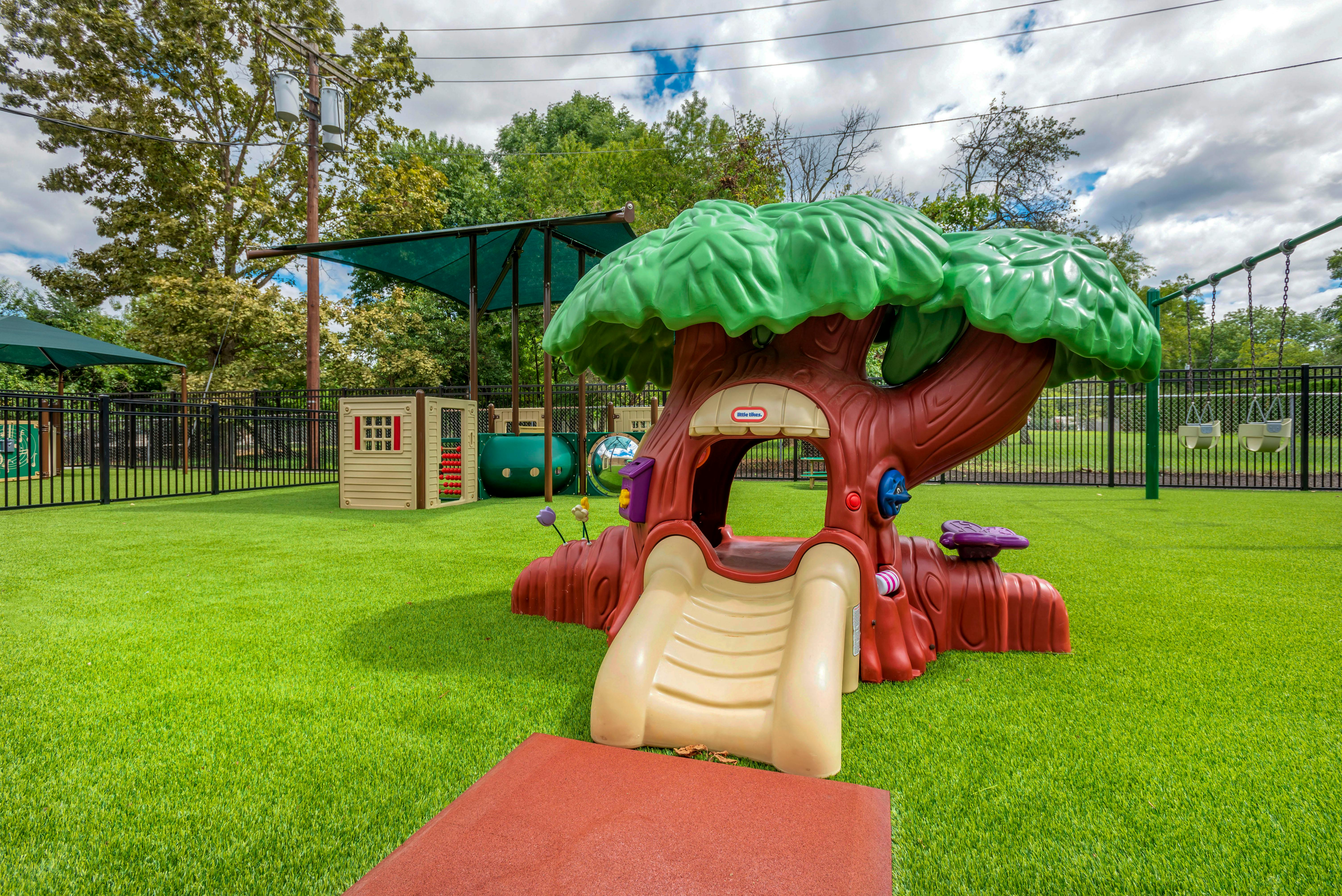 Little Tikes playground on artificial grass with swings and fence
