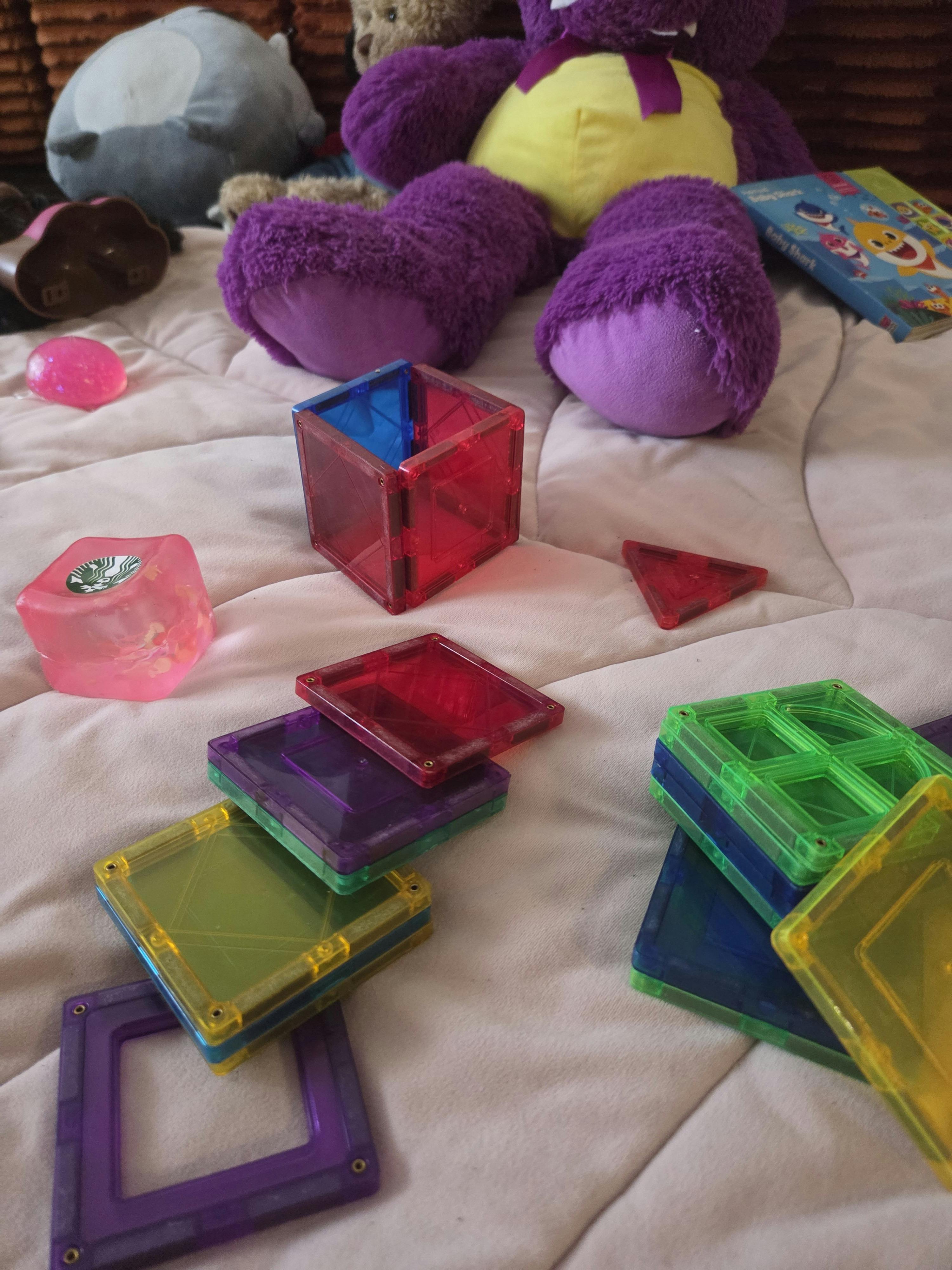 Colorful magnetic building tiles and stuffed animals on a soft surface