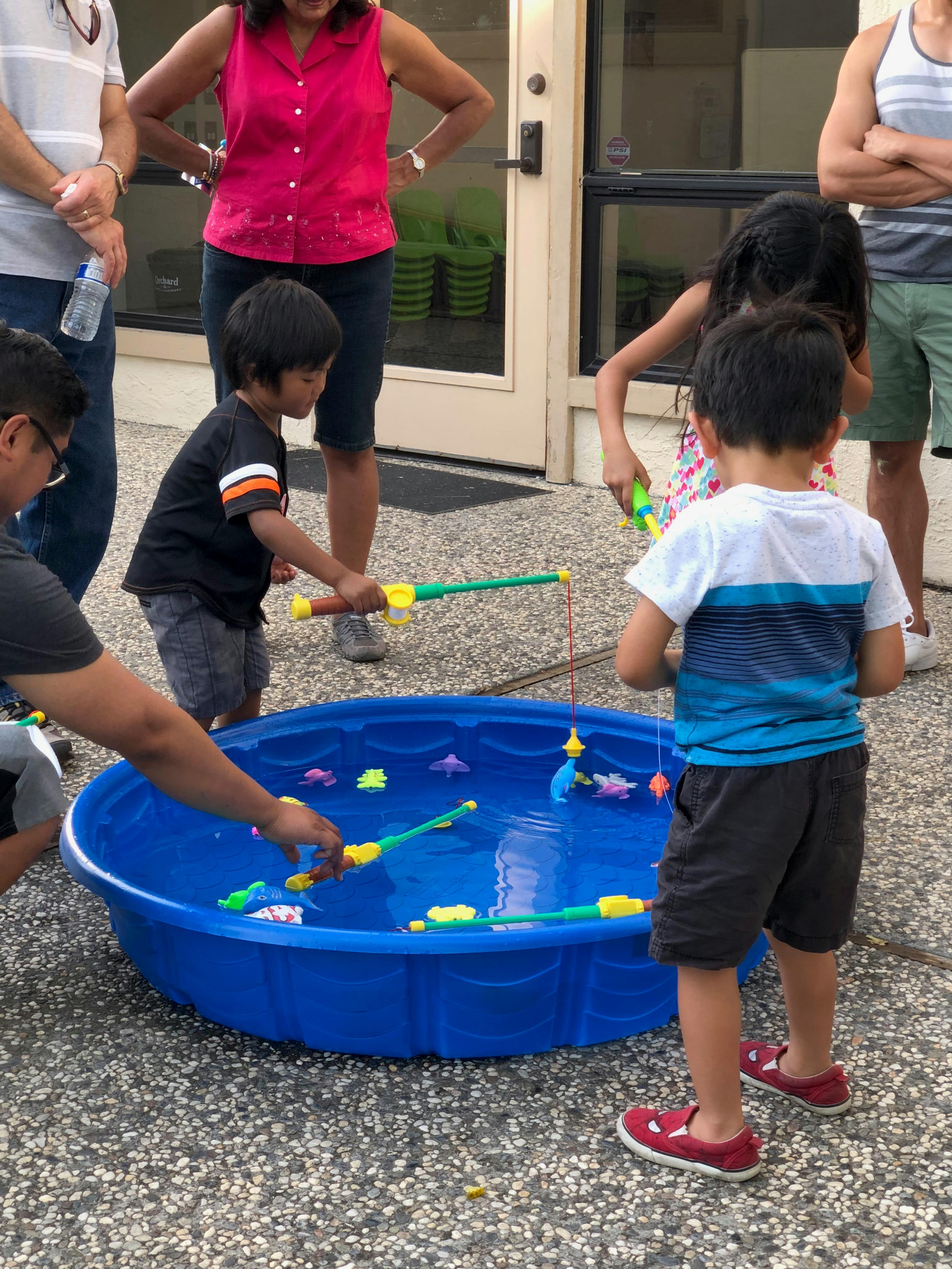 Children playing a fishing game in a blue pool with adults nearby