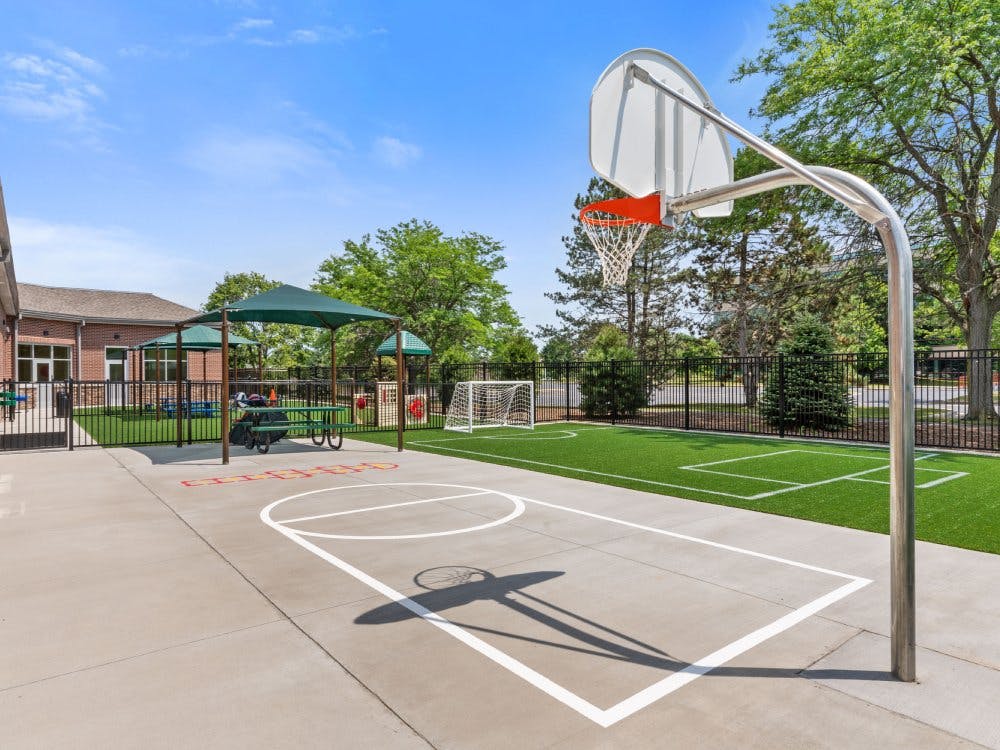 Basketball hoop on a paved court next to a fenced turf play area