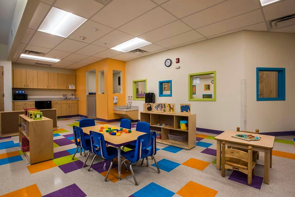 Classroom with small tables and chairs, colorful floor tiles, and a kitchen area
