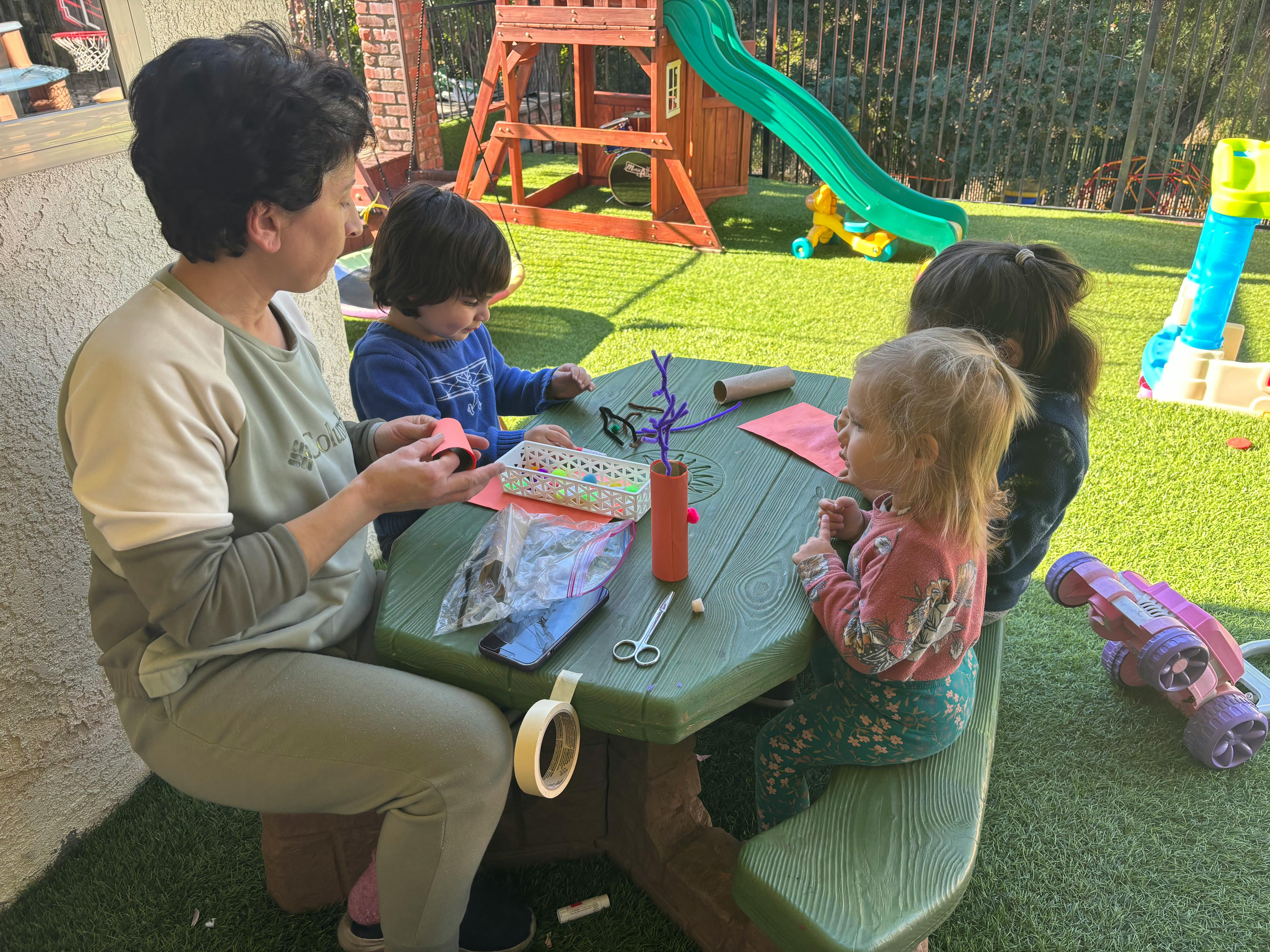 Adult and children doing crafts at a picnic table outdoors