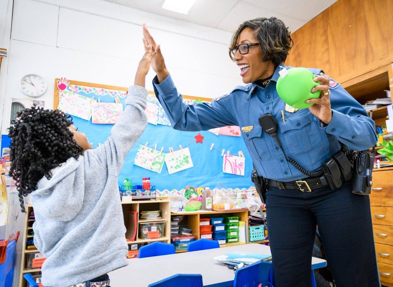 Adult in uniform giving a high five to a child in a classroom