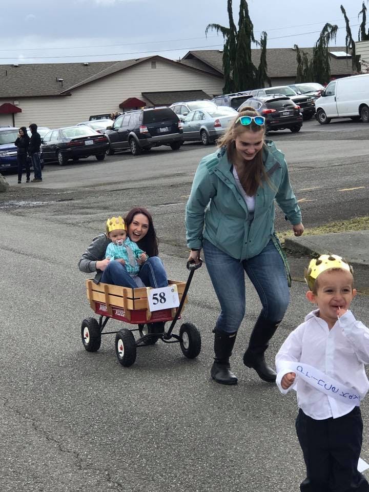 Two people pulling a child in a wagon, another child running