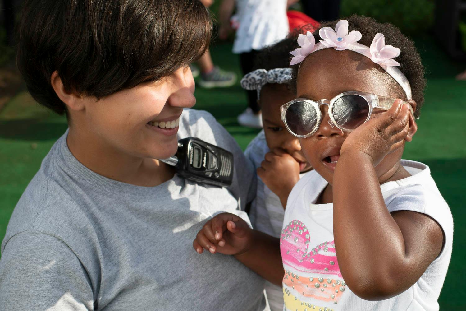 Person smiling at a child wearing sunglasses and a flower headband