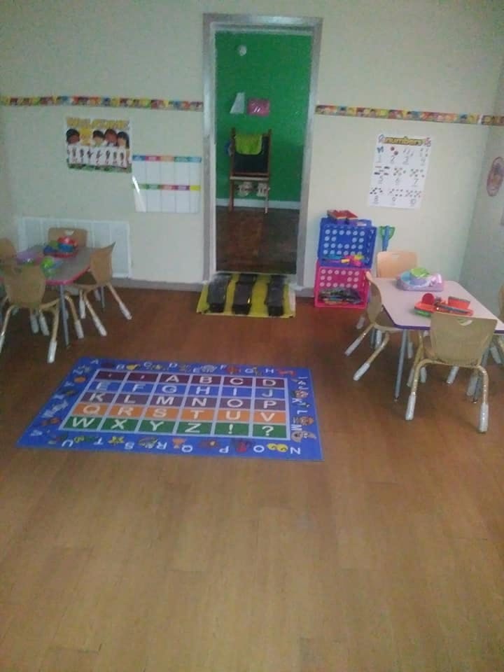 Classroom with small tables and chairs, an alphabet rug, and a green door