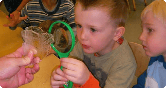 Child looking through a magnifying glass at an object held by an adult