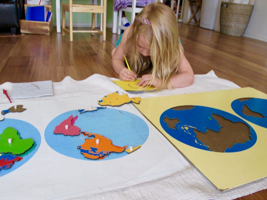 Child drawing while lying on the floor with world map puzzles