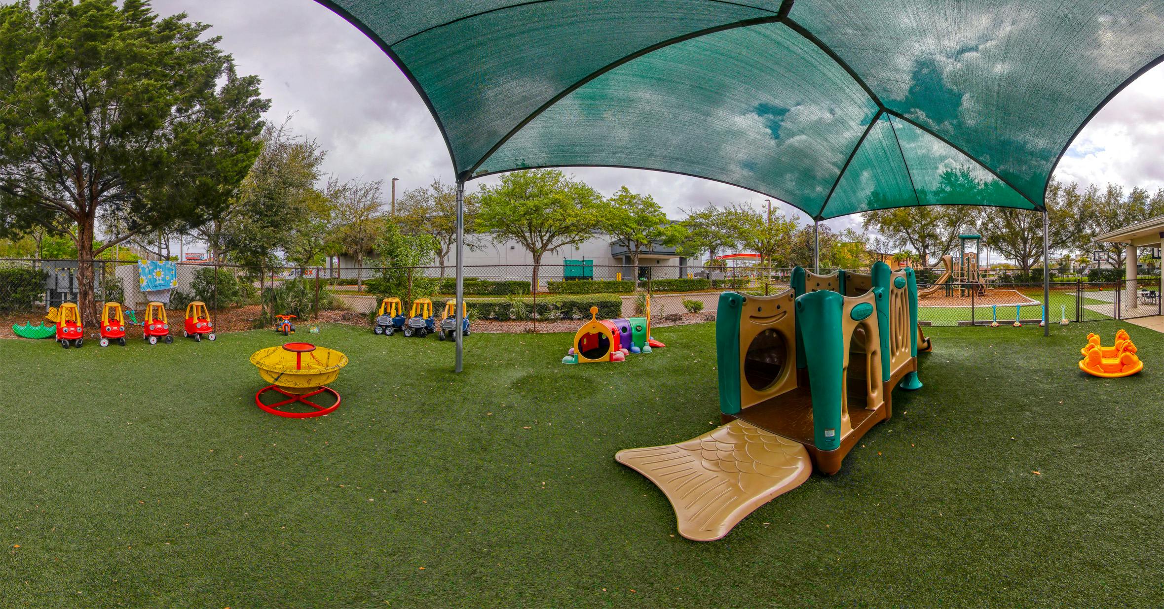 A children's playground with artificial turf under a large green shade