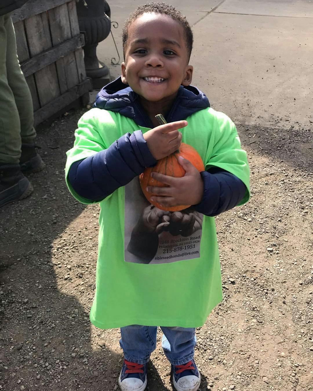 Child holding a small pumpkin and pointing