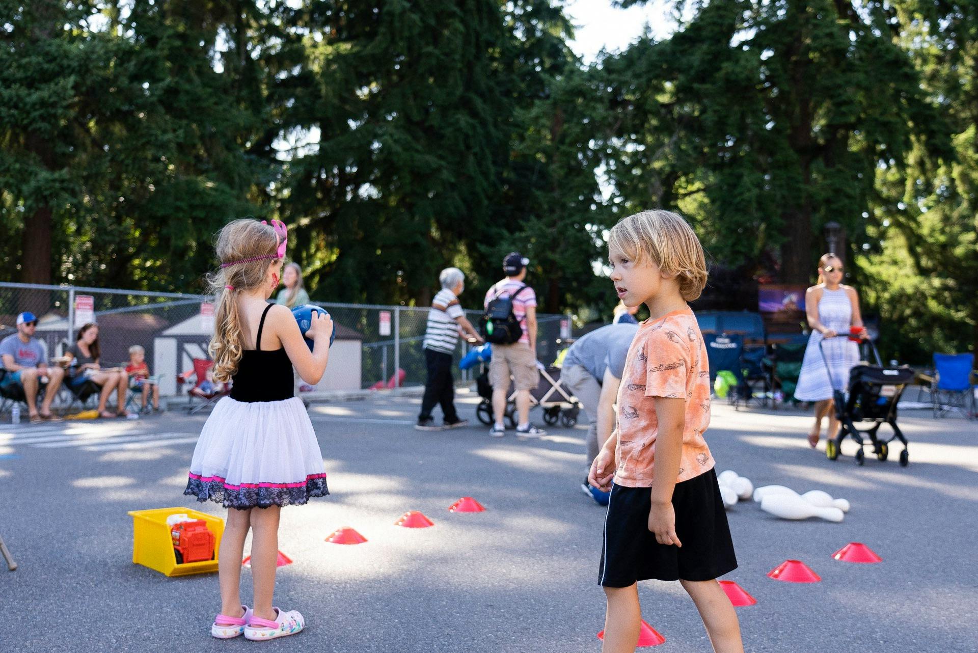 Child holding a ball while standing near another child and orange cones